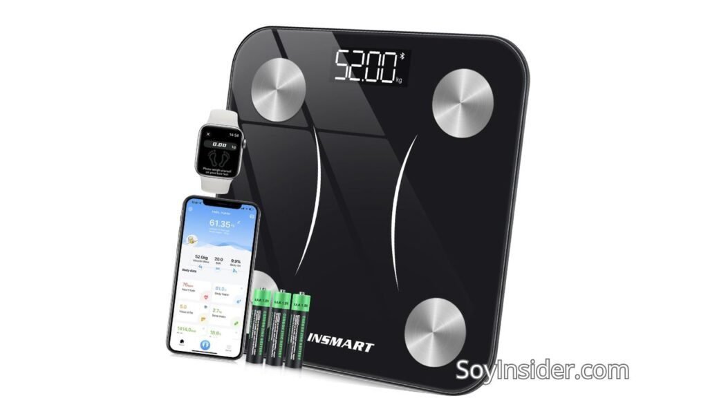 Una báscula inteligente de baño de color negro con diseño moderno, equipada con cuatro sensores metálicos en las esquinas para medición de datos corporales. La pantalla digital integrada muestra un peso de "52.00 kg". Junto a la báscula, hay un smartwatch y un teléfono móvil mostrando la sincronización con la báscula, donde se leen datos como "61.35 kg", "20.0 % grasa corporal" y otros indicadores de salud. También se observan cuatro pilas AAA frente a la báscula. En la parte inferior derecha de la imagen aparece la marca "SoyInsider.com".