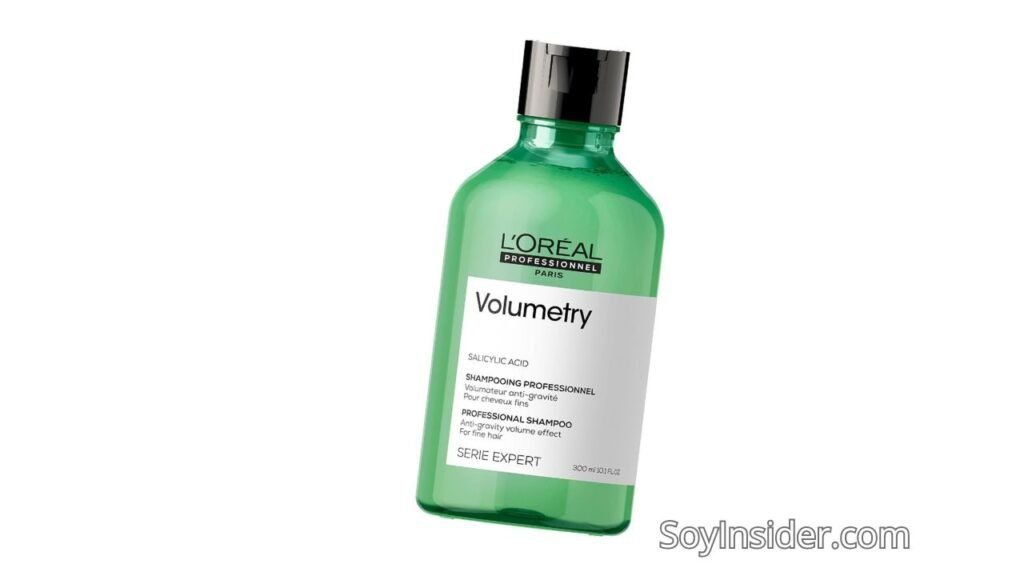 Imagen de una botella verde con tapa negra del champú L’Oréal Professionnel Volumetry. La etiqueta blanca en la parte frontal detalla el producto como un champú profesional diseñado para cabello fino, proporcionando un efecto de volumen antigravedad. El envase tiene un diseño elegante y profesional, resaltando la calidad del producto. En la parte inferior derecha de la imagen aparece la marca "SoyInsider.com".