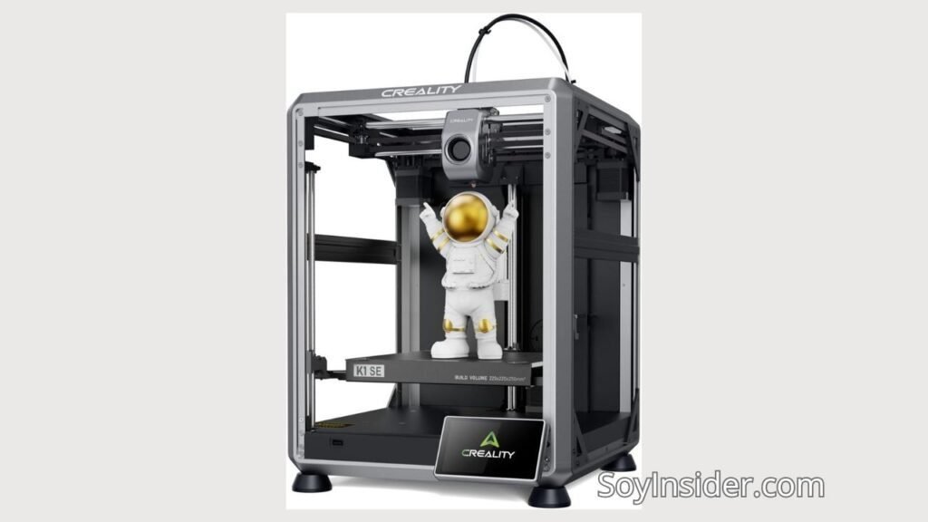Impresora 3D de la marca Creality modelo K1 SE, con un diseño de marco metálico abierto y estructura robusta. En el interior de la impresora, se muestra una figura de un astronauta blanco con detalles dorados que parece estar en proceso de impresión. En la parte inferior, una placa con el logotipo de Creality. Sobre el recuadro de la base se puede leer: "Build Volume 220x220x250mm". En la esquina inferior derecha de la imagen se encuentra el texto "SoyInsider.com".