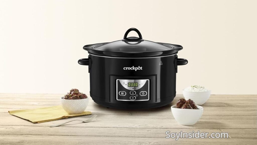 Olla de cocción lenta Opiniones de usuarios, sus ventajas y desventajas y los mejores. en la imagen Una olla de cocción lenta Crockpot negra colocada sobre una mesa de madera clara, acompañada de tres pequeños cuencos blancos con comida y un paño amarillo con utensilios. El fondo es minimalista con tonos beige. En la parte inferior derecha de la imagen aparece la marca "SoyInsider.com".